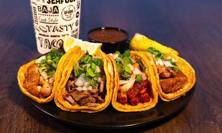 4 brightly lit tacos on a plate served with peppers and lemons.