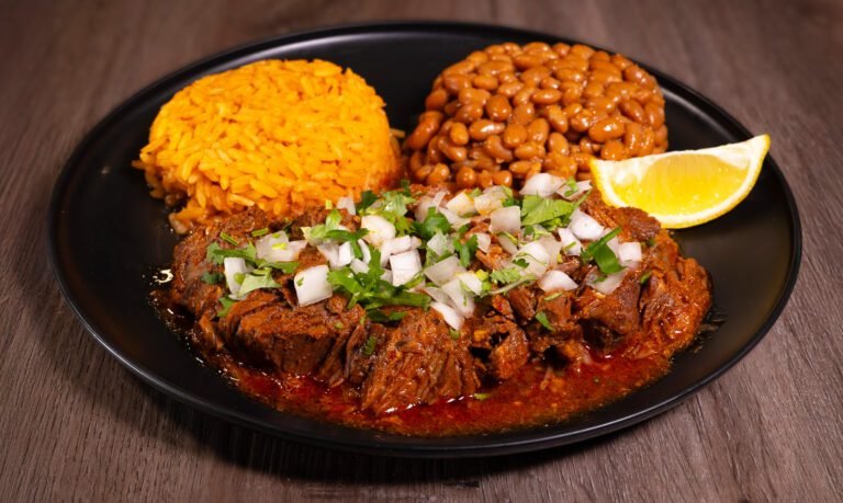 plate of birria with rice, beans, onions, cilantro, and a fountain drink
