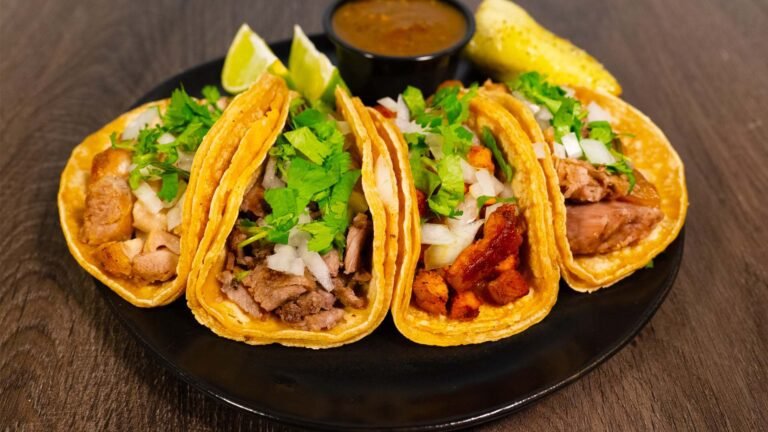 4 brightly lit tacos on a plate served with peppers and lemons.