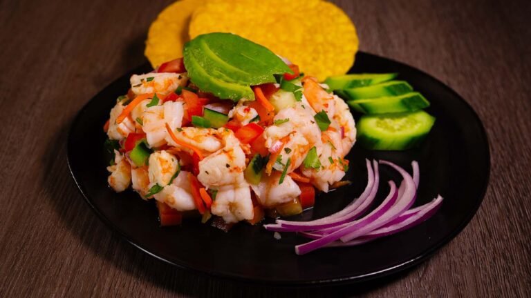 a neatly prepared shrimp ceviche with vegetables on top and to the side as well as tostada all on a plate.