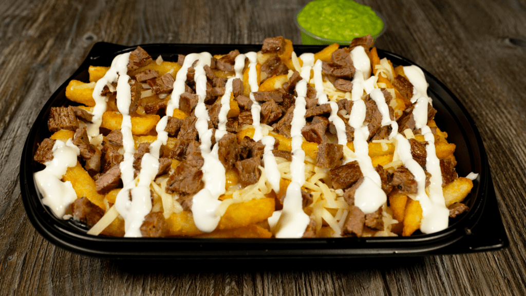 asada fries on a table topped with sourcream and a side of guacamole.
