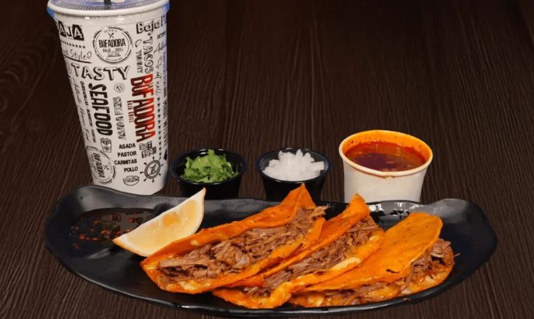 A plate of quesabirria tacos with lemon, salsa, and onions, cilantro, a drink