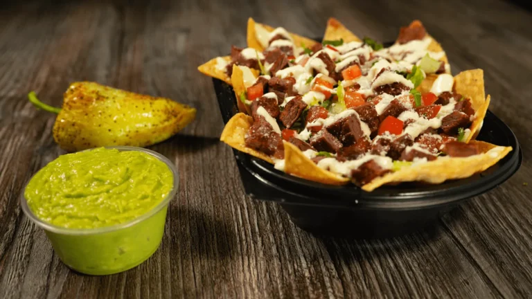 Baja nachos topped with carne asada, pico de gallo and house cream, with a side of guacamole and a roasted chile